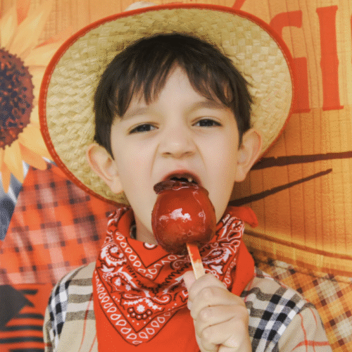 Young boy eating a candied apple in fall clothing